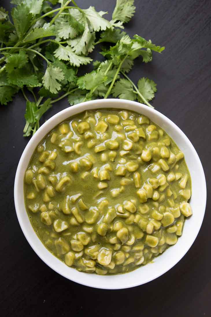 Best vegan meal on VG in 2017. Overhead photograph of green indian coconut curry with corn served in a round white bowl, garnished with cilantro on the side. 