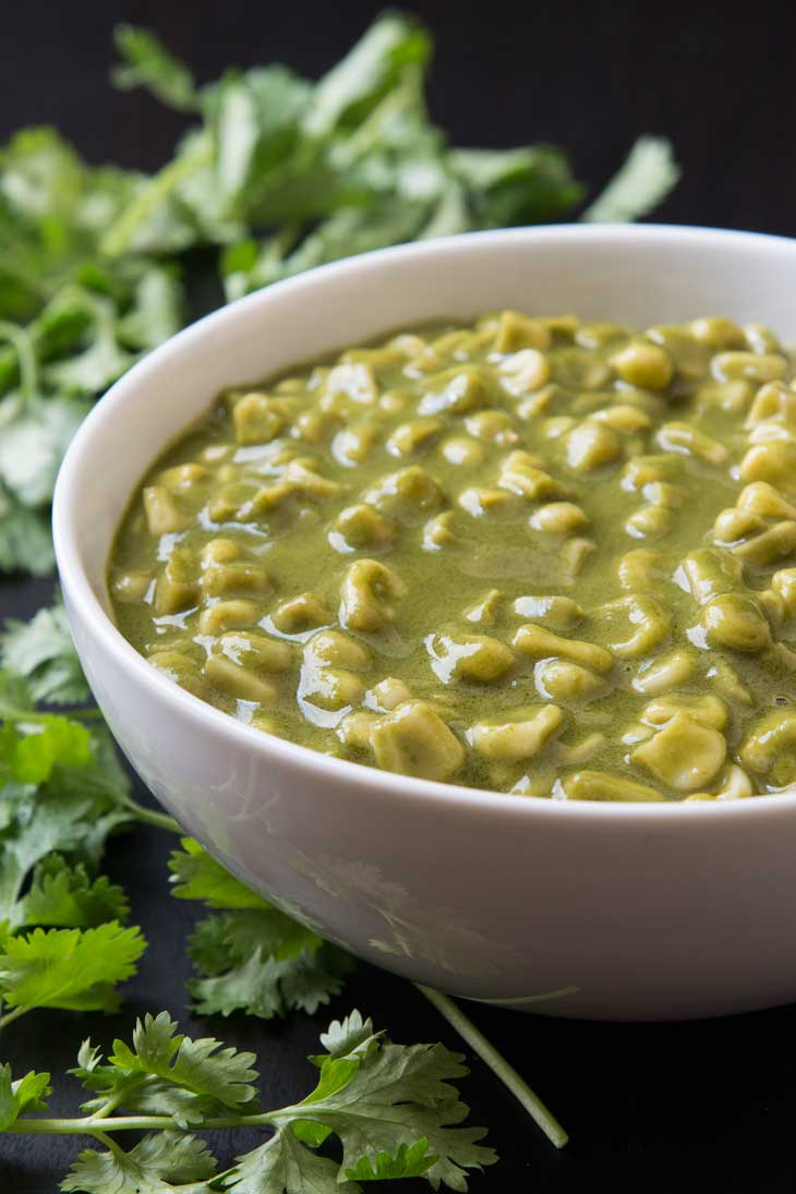 A side close-up photograph of green vegan indian curry with corn served in a white bowl and garnished with cilantro. 