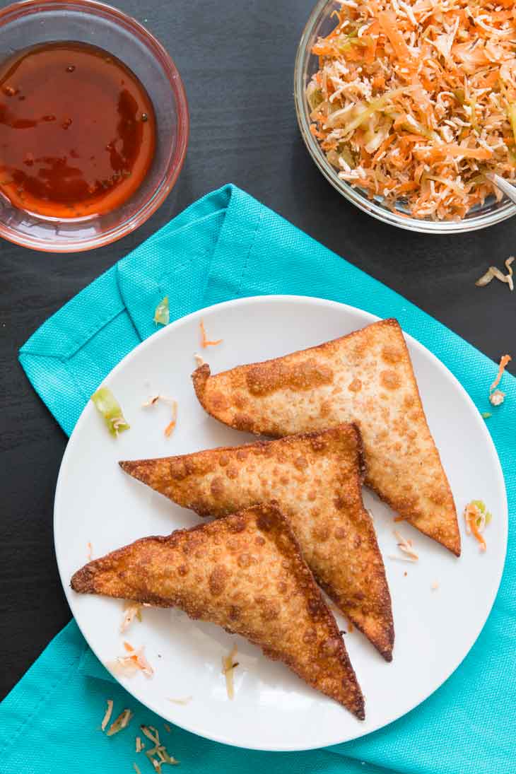 Overhead photograph of how to make wontons. 3 crispy wontons on a white plate, sitting on a blue napkin.