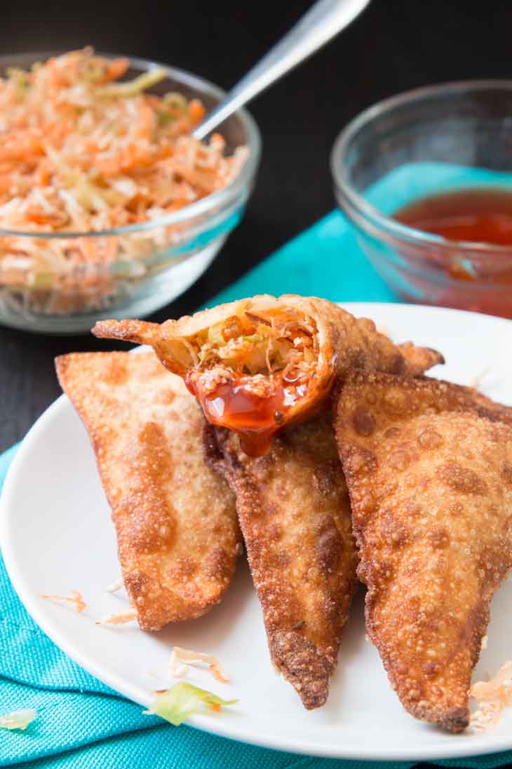 A side photograph of vegan crispy wontons sitting on a white plate, dipped in sweet and sour sauce.