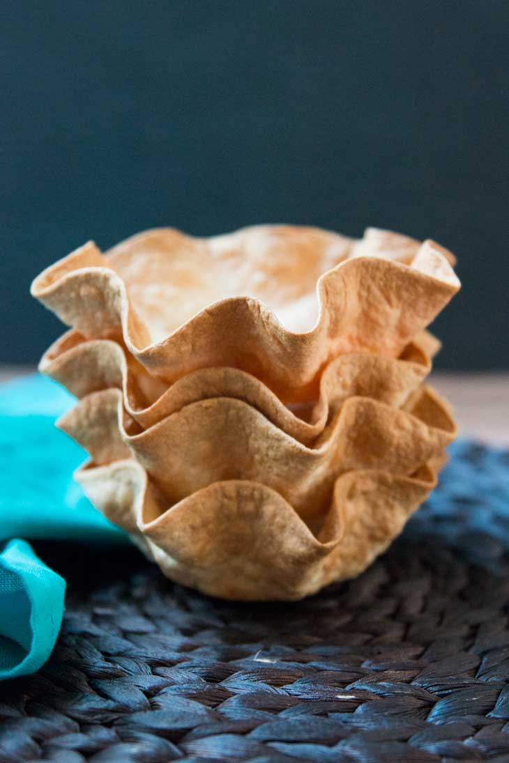 A photograph of four baked tortilla bowls stacked on top of each for layered taco salads. They are sitting on a dark brown place mat. 