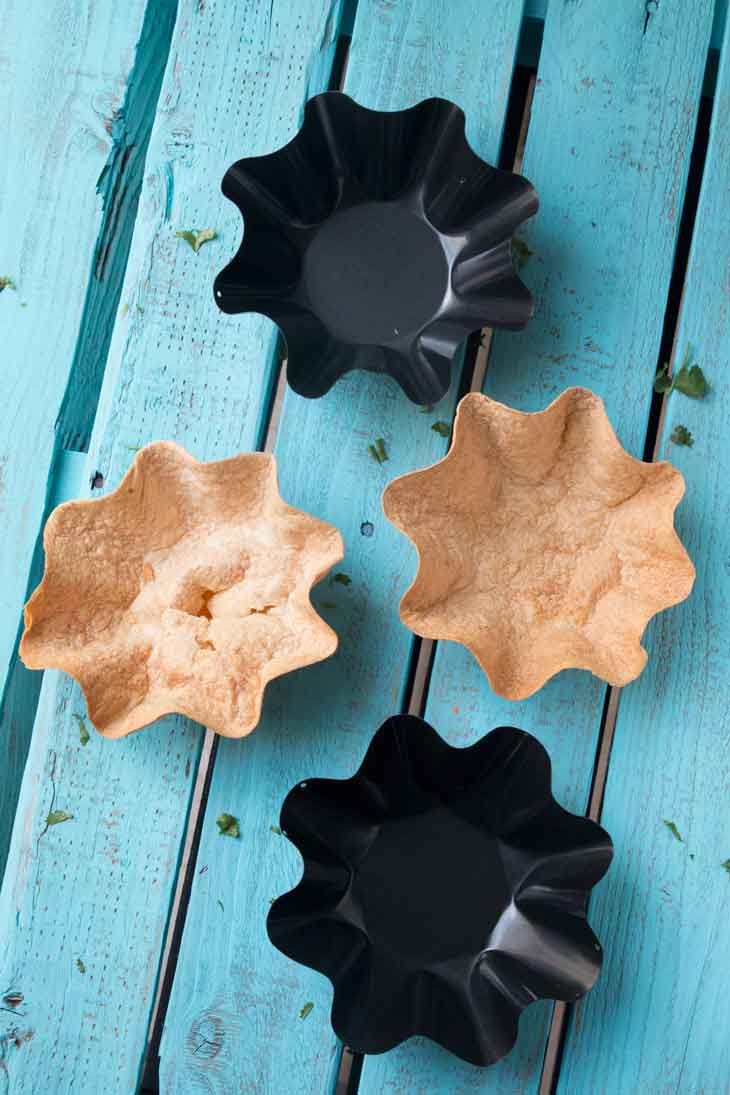 An overhead photograph of two non-stick tortilla bowl molds and two baked tortilla bowls for layered taco salads. 