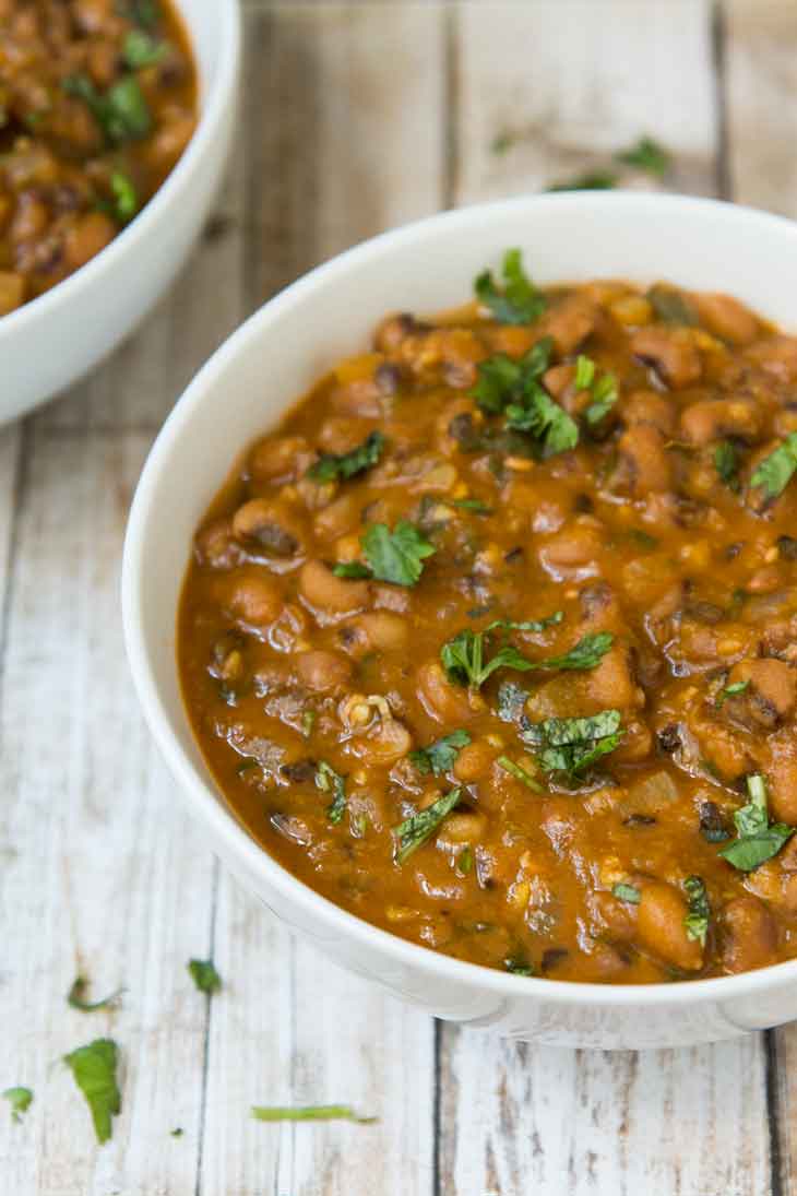 A side photograph of vegan black eyed peas recipe in a round white bowl. It's sitting on a white wooden board and garnished with fresh cilantro.