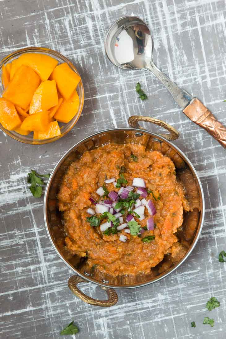 Overhead photograph of pav bhaji masala recipe. There's a bowl of fresh mango and copper spoon off to the side with fresh cilantro as garnish. 