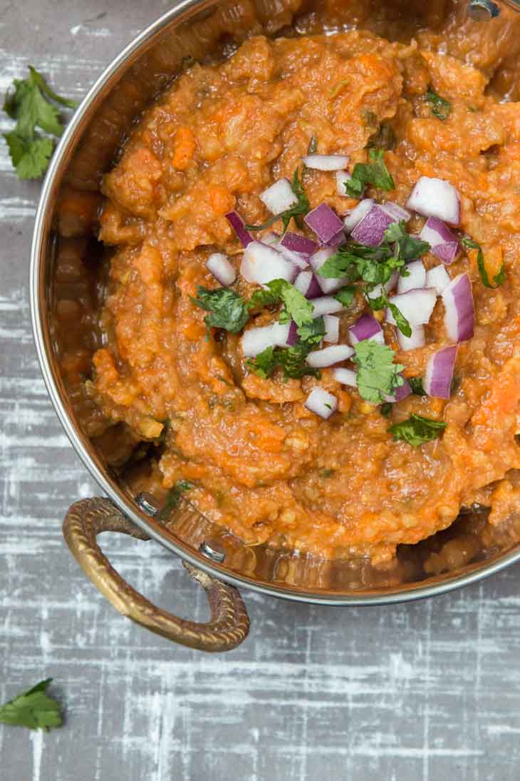 Overhead closeup of pav bhaji masala recipe in a copper bowl topped with onions and cilantro. 