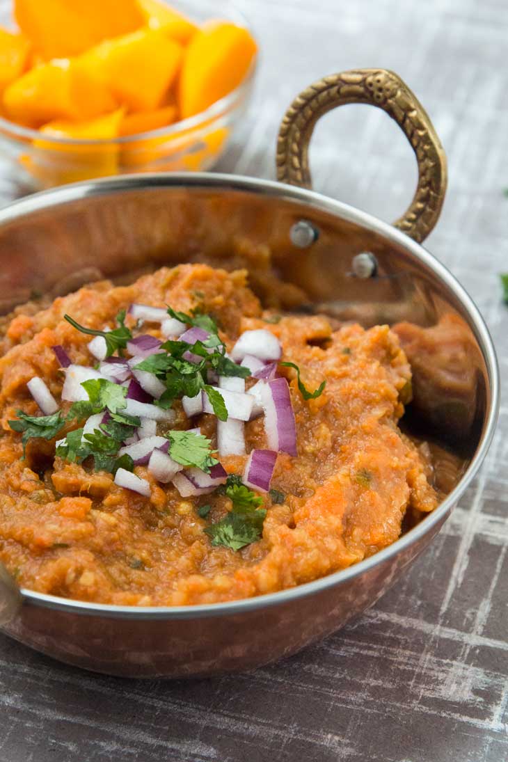 A 45 degree photograph of Pav Bhaji Masala recipe in a copper traditional bowl with a side of fresh mango in the background.