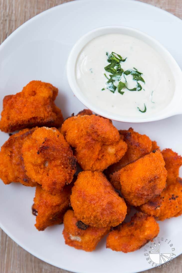 An overhead photograph of roasted buffalo cauliflower sitting on a round white plate, served with vegan cucumber ranch dressing.