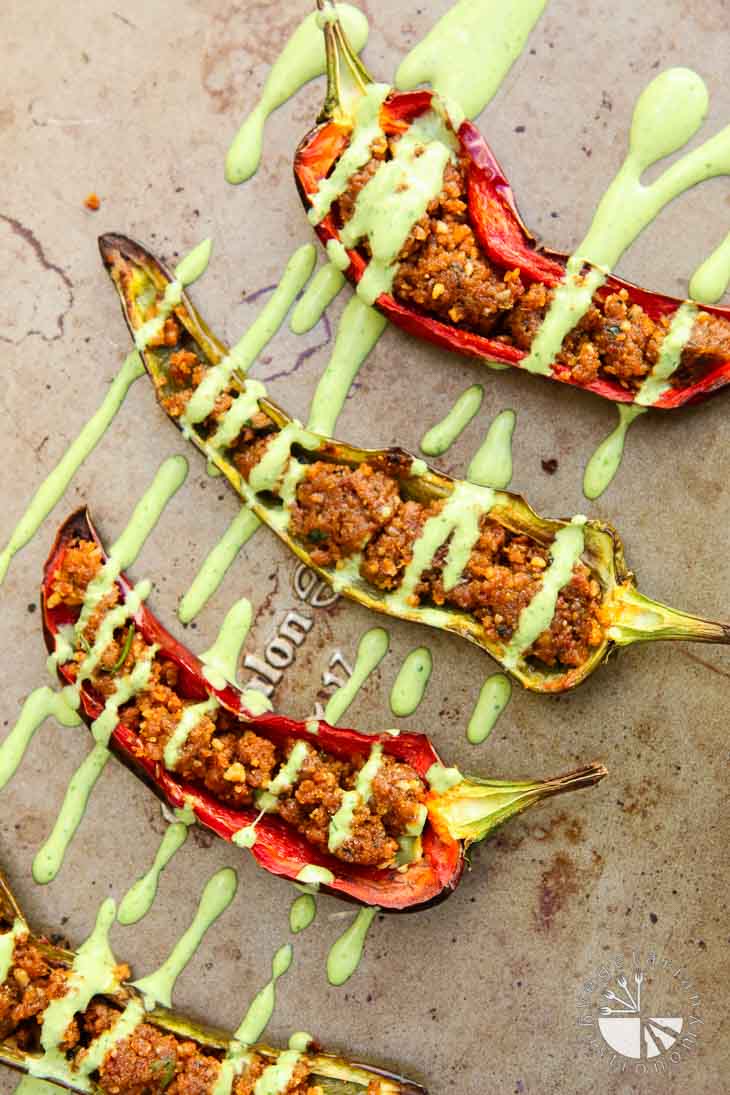 An overhead photograph of stuffed anaheim peppers with cilantro tahini sauce drizzled on top. They are sitting on a baking sheet.