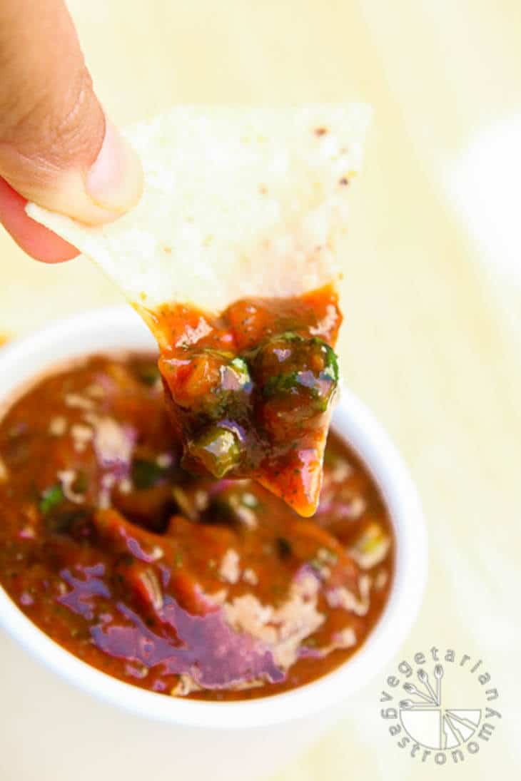 A side view of someone holding a chip dipped in chunky tomato salsa.