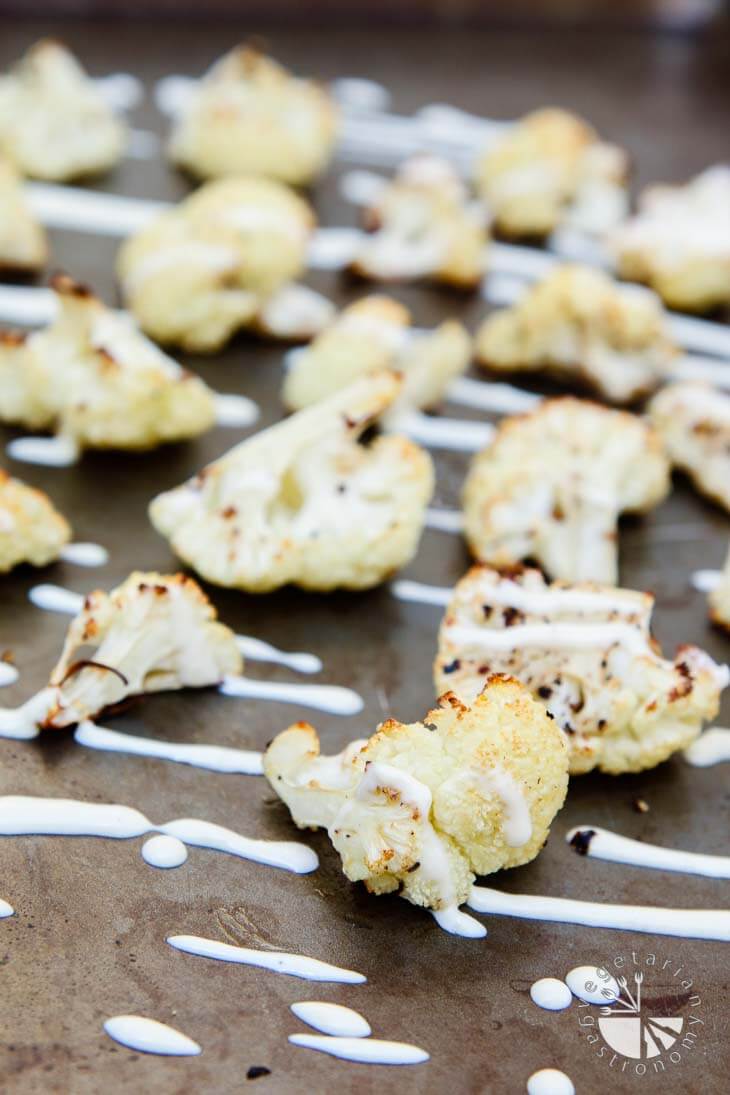 A side view of roasted cauliflower sitting on a baking sheet drizzled with garlic lime tahini sauce.