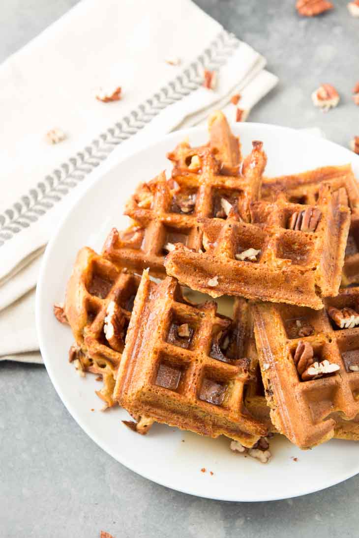 Side photoograph of pumpkin vegan waffles with pecans scattered on top.