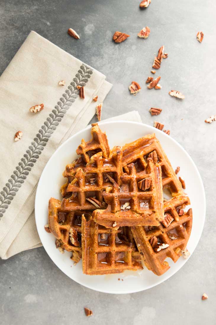 Overhead photograph of pumpkin vegan waffles on a white plate with pecans scattered on top.