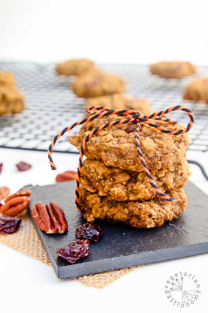 A front view photograph of three stacked pumpkin pecan cookies tied together with a string. There are additional cookies sitting on a cooling rack in the background out of focus. 