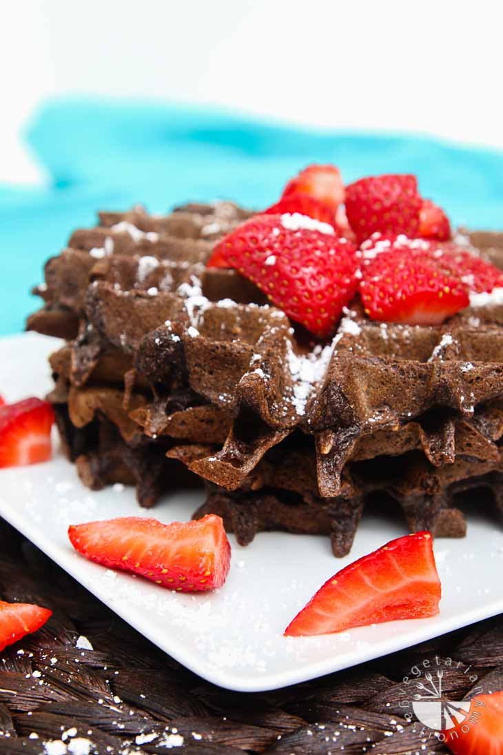 A front view of double chocolate strawberry waffles. It consists of two stacked waffles topped with powdered sugar and strawberries. 