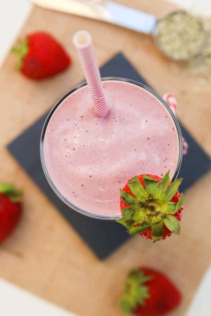 Overhead photograph of strawberry milkshake recipe with hemp seeds and strawberries in the background.