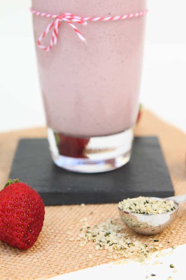 Closeup of hemp seeds and fresh strawberries being used in a vegan strawberry milkshake recipe.