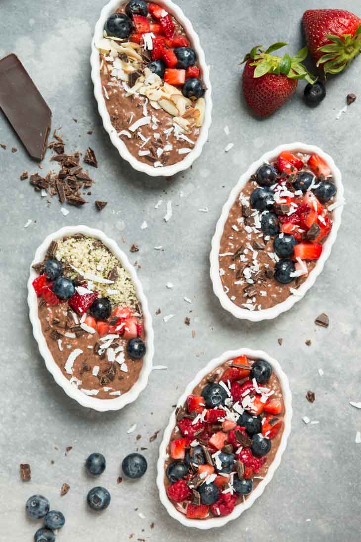 Overhead photograph of 4 small chocolate chia pudding pies topped with fresh fruit, nuts, and coconut.