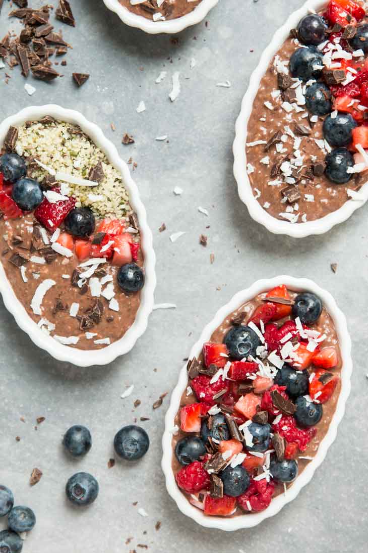 An overhead close-up of single serving chocolate chia pudding pie, with blueberries, chocolate, and coconut scattered around.