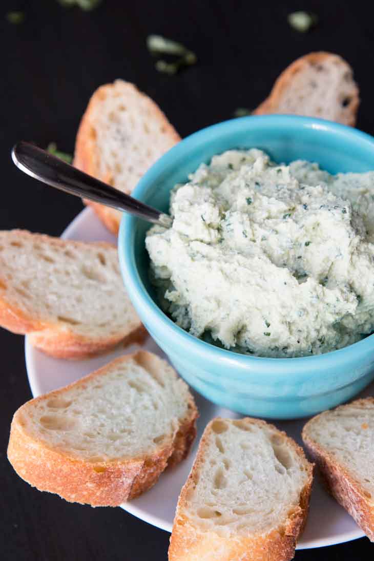 Side photograph of vegan tofu ricotta spread plated in a blue bowl and surrounded by slices of french bread.