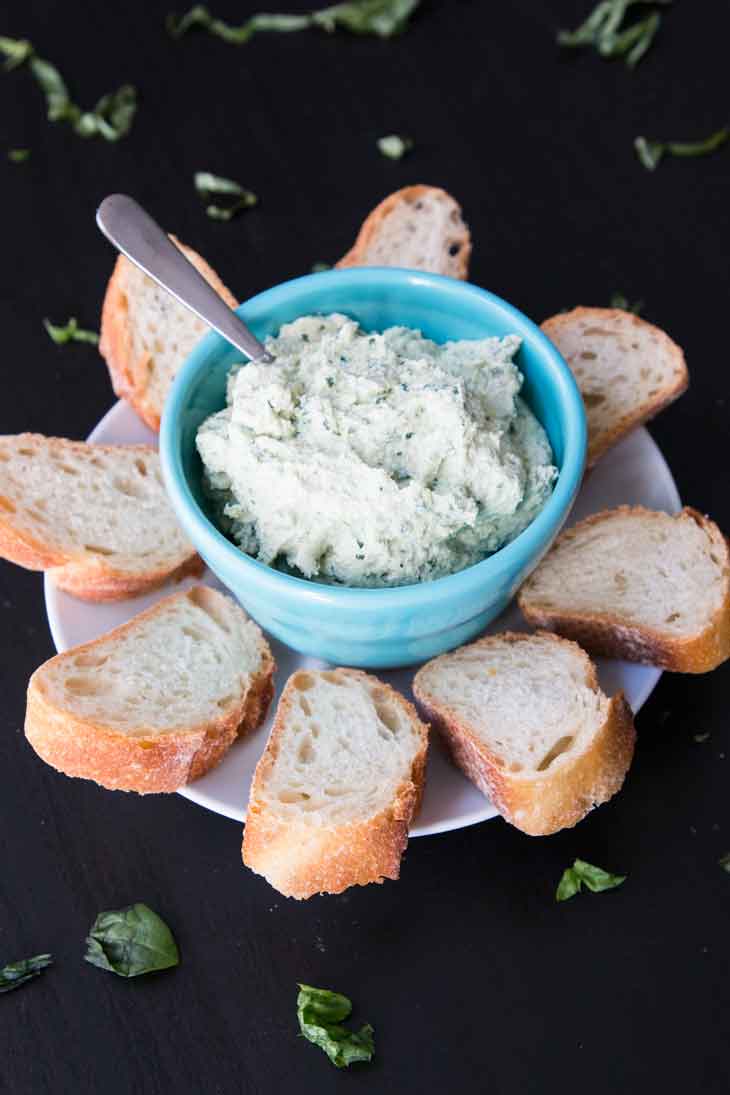 A side photograph of vegan tofu ricotta plated in a blue bowl, with slices of french bread and garnished with fresh basil.