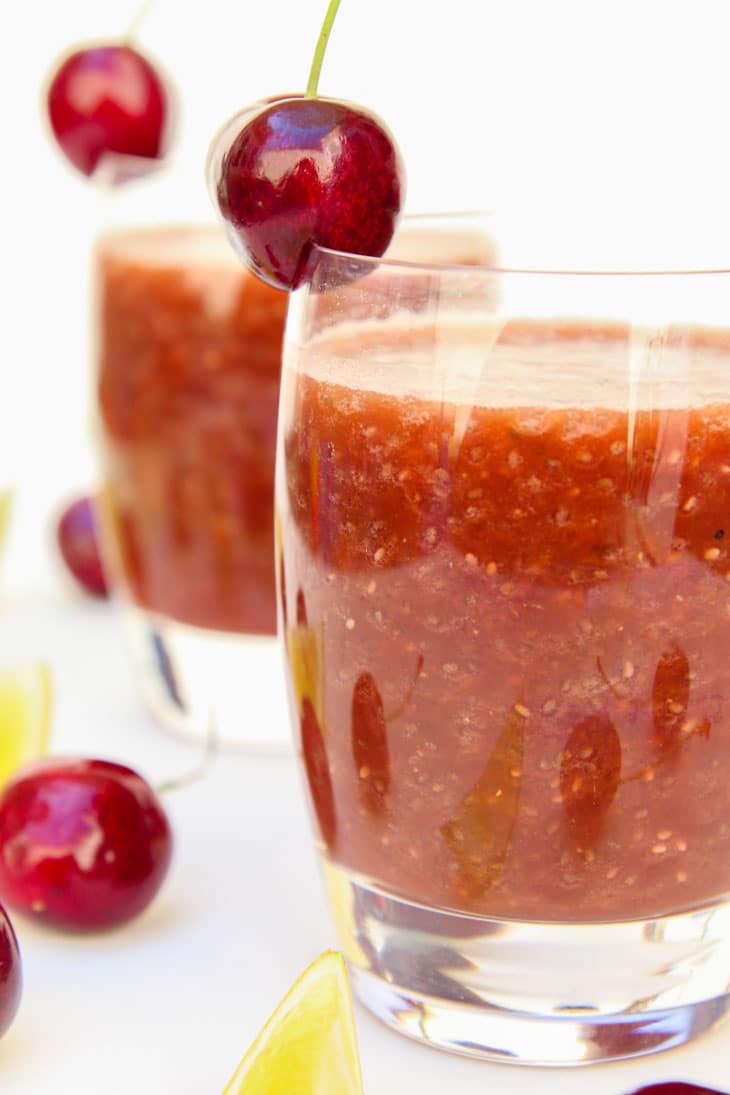 A side shot of a glass of cherry chia fresca topped with a fresh cherry