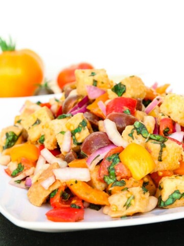 A side shot of a tuscan panzanella salad with white beans on a white plate