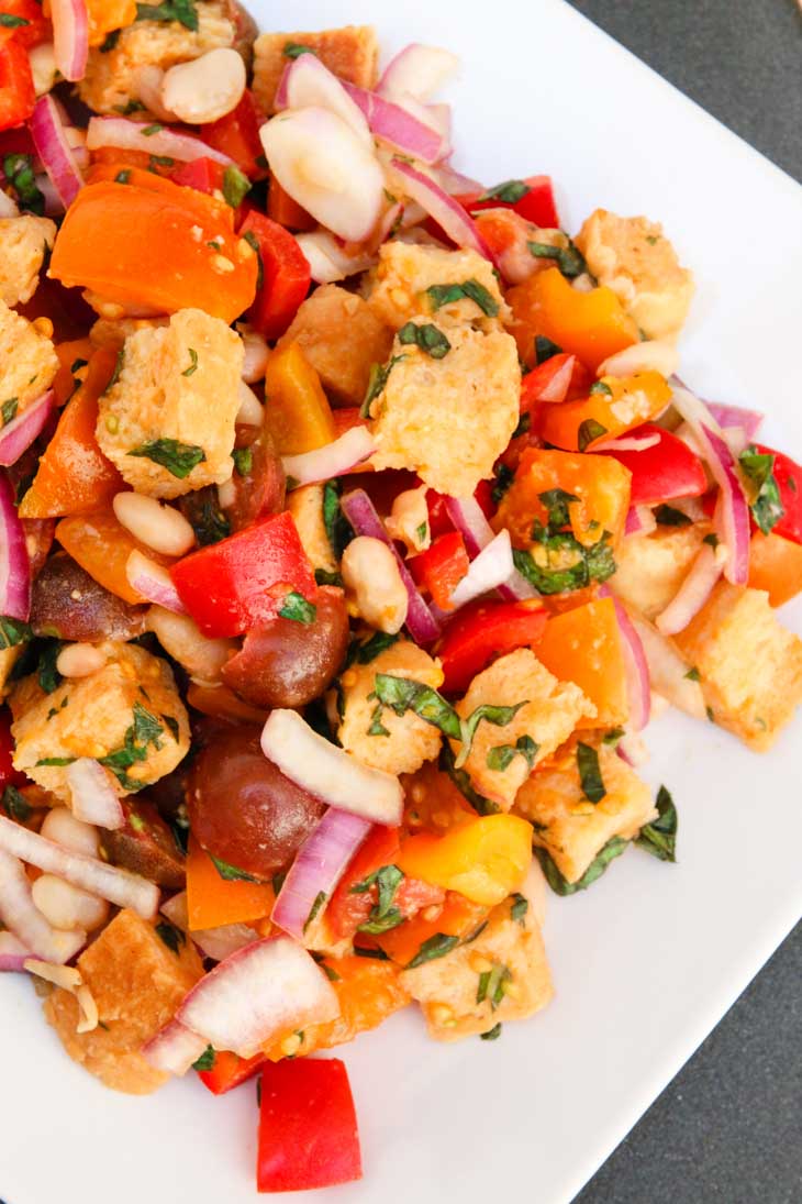 A tuscan panzanella salad with white beans on a white plate garnished with basil