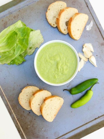 An overhead shot of spicy green peruvian sauce on a tray with slices of bread at the side