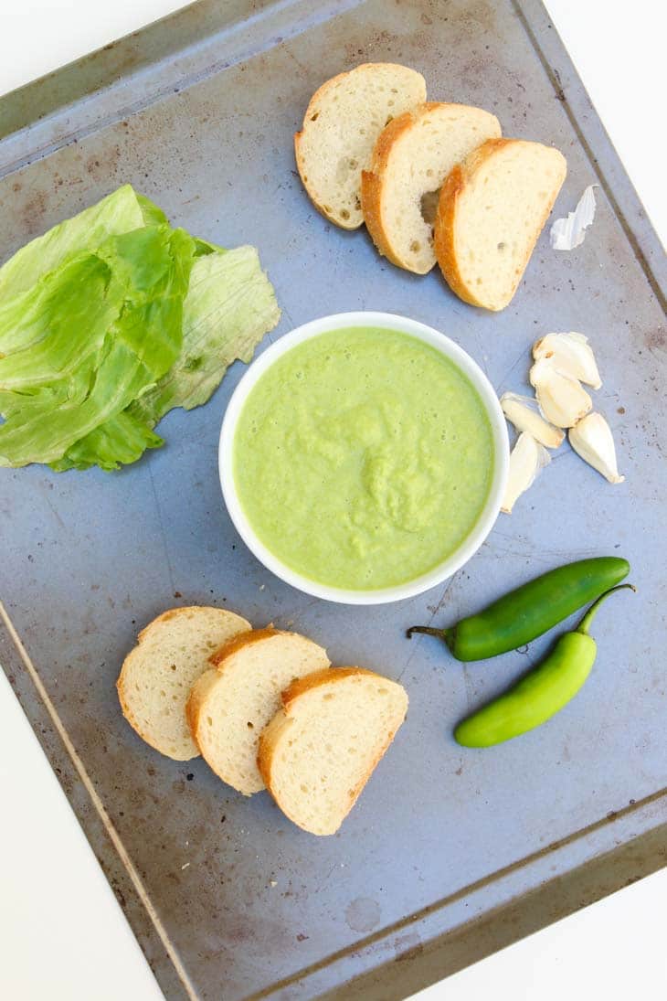 An overhead shot of spicy green peruvian sauce on a tray with slices of bread at the side