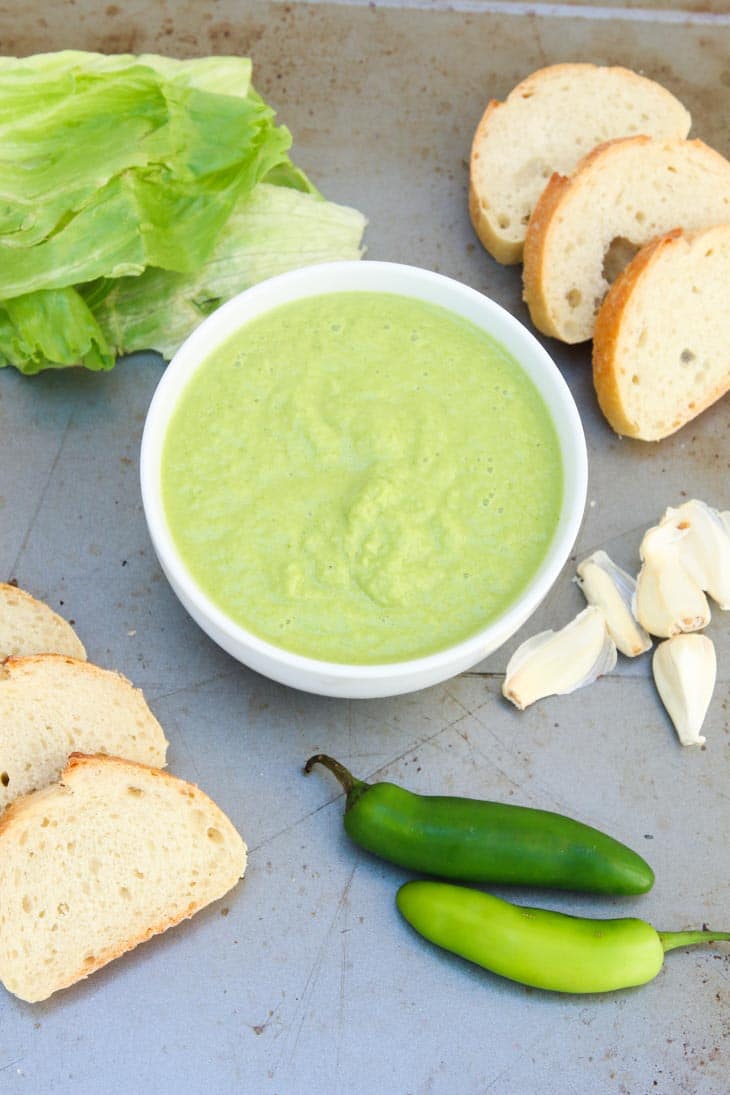 Spicy green peruvian sauce in a white dish with slices of bread and lettuce at the side