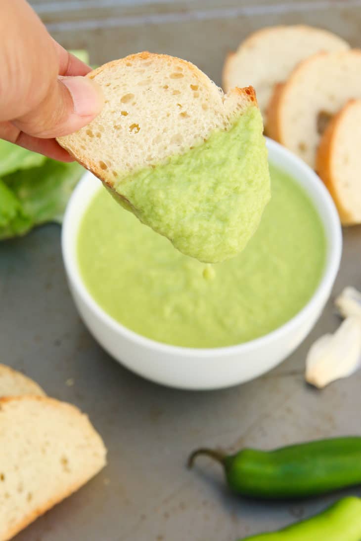 Someone dipping a slice of bread into spicy green peruvian sauce