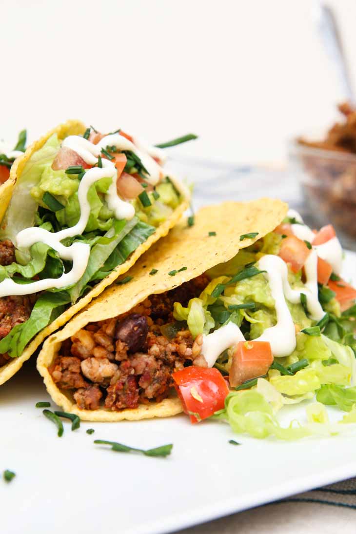 A photograph of two loaded vegan black bean tofu tacos laying on the side and sitting on a white plate.