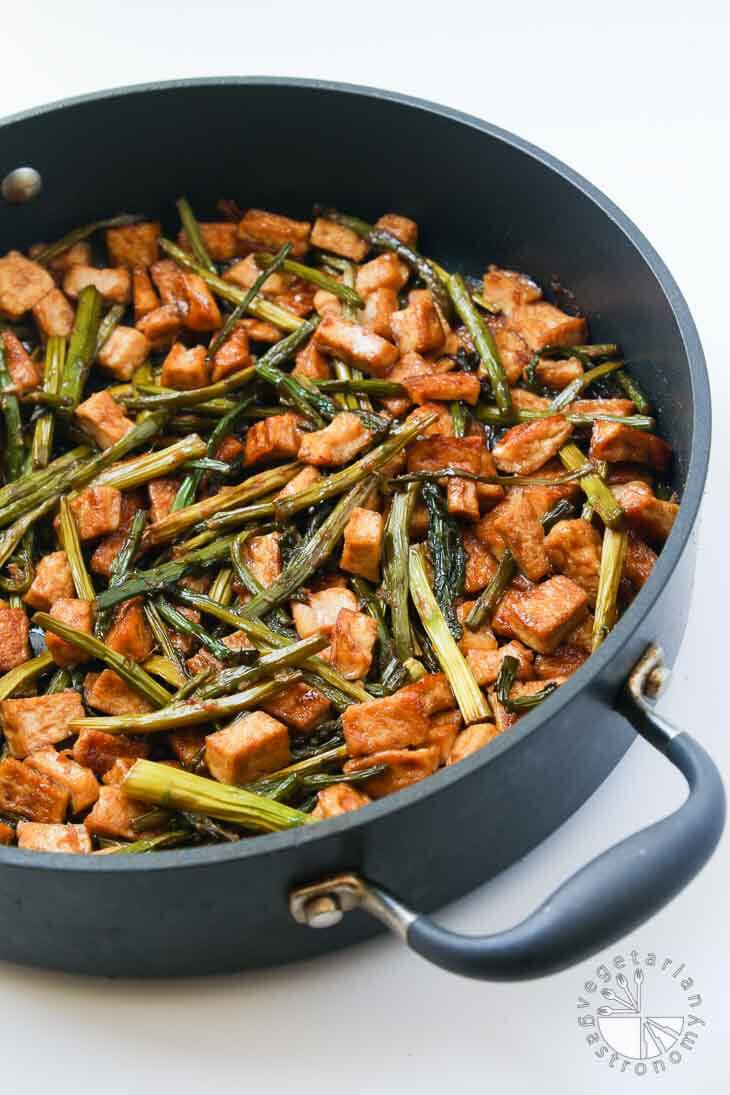 A side 45 degree partial view of a large non-stick black pan containing Teriyaki tofu stir fry with asparagus. 