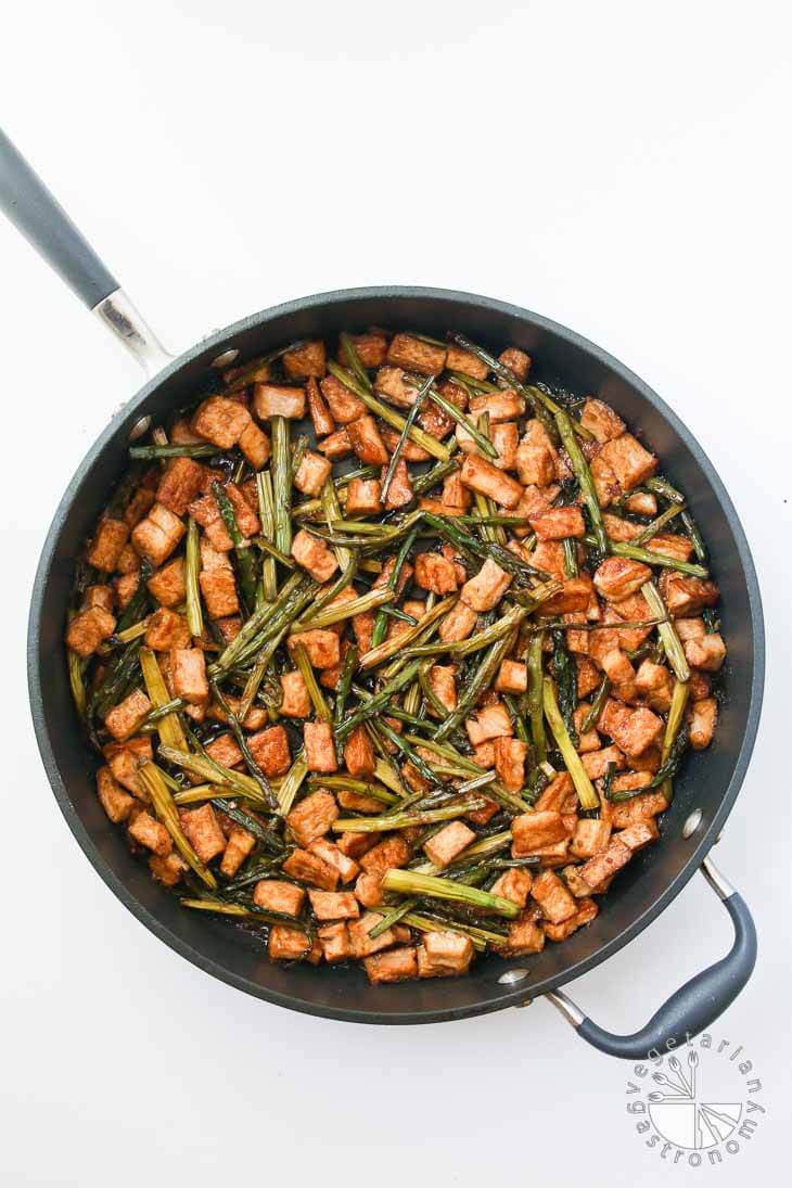 An overhead shot of a large non-stick black pan containing Teriyaki Tofu stir fry with asparagus. The pan is sitting on a white board.