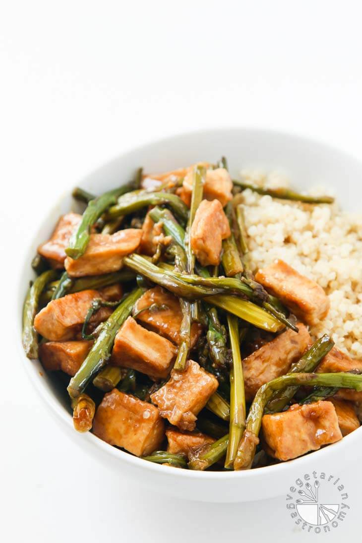 Front photograph of a white bowl containing Teriyaki Tofu stir fry with asparagus and cooked quinoa. 