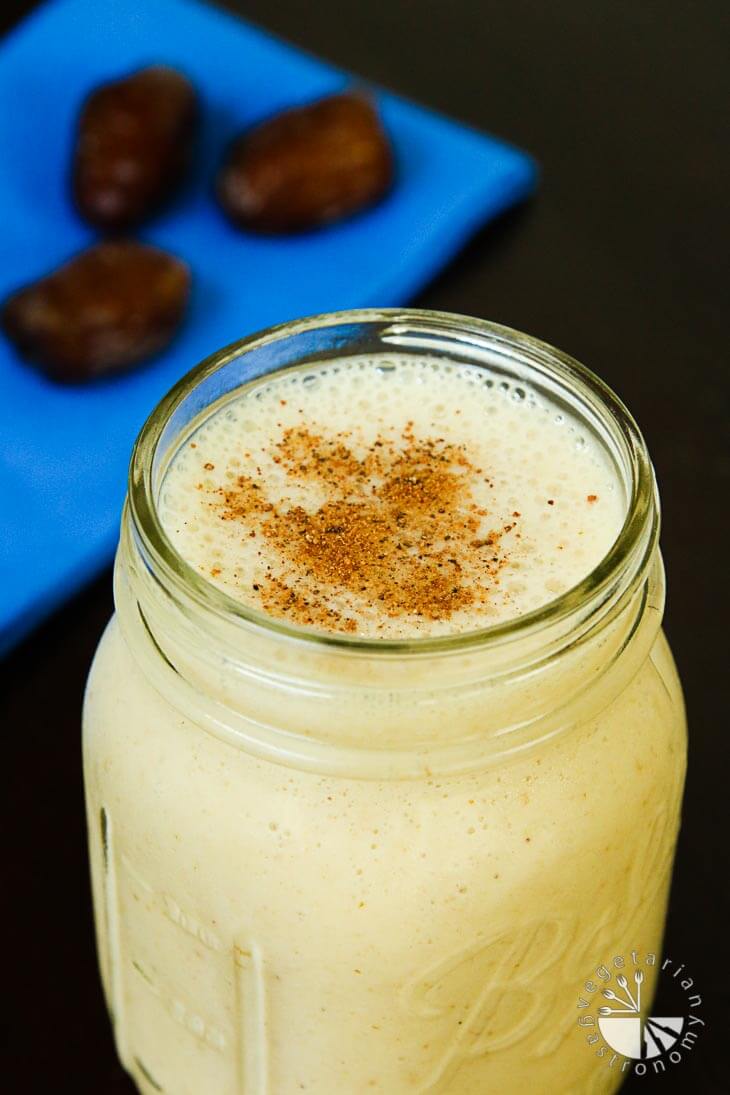 A side photograph of a date shake in a mason jar with dates out of focus in the background on a blue napkin.