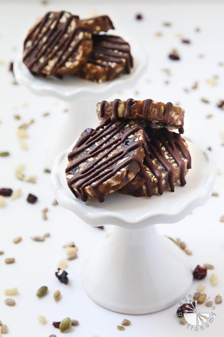 A side photograph of no-bake date cookies. There are 2 sets of 3 cookies on a white holder with nuts and dried fruit scattered around.