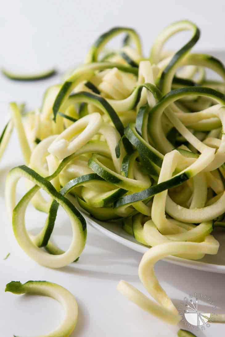 A side photograph of spiralized zucchini spaghetti on a white plate.