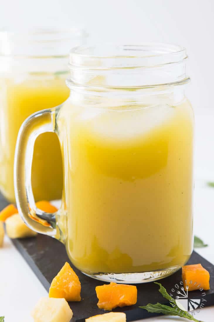 A side view of a mason jar filled with pineapple mango agua fresca recipe with fresh fruit garnished around the sides.