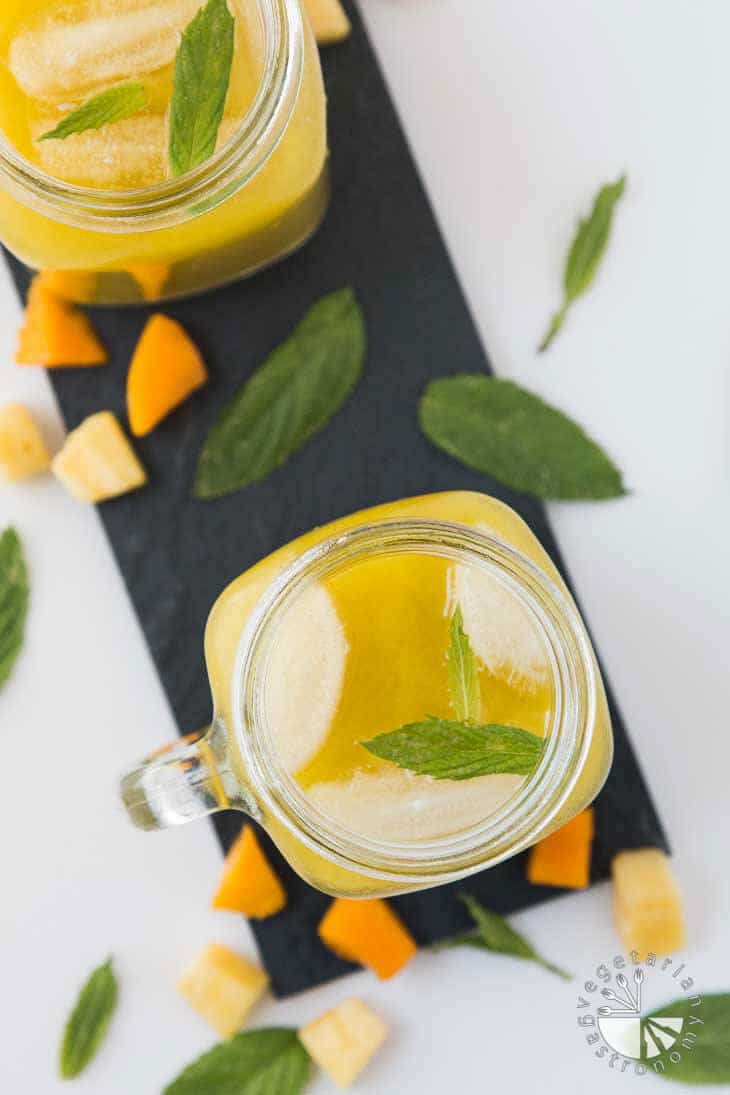 An overhead closeup of a mason jar filled with pineapple mango agua fresca recipe, with fresh fruit and mint scattered around the sides.