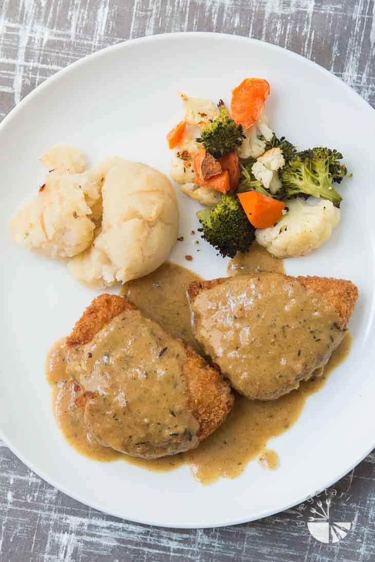 An overhead photograph of Country Fried Chick'N consisting of vegan chicken topped with gravy and a side of potatoes and roasted veggies. 