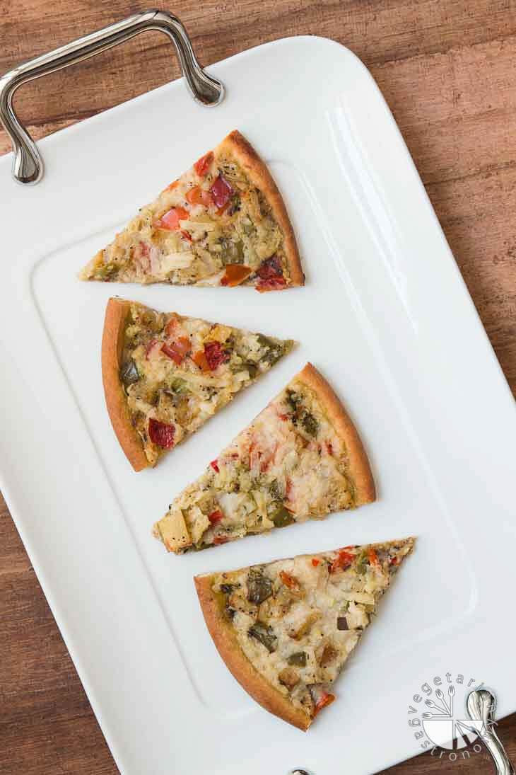 An overhead photograph of veggie pesto pizza cut into triangles, sitting on a white tray. 