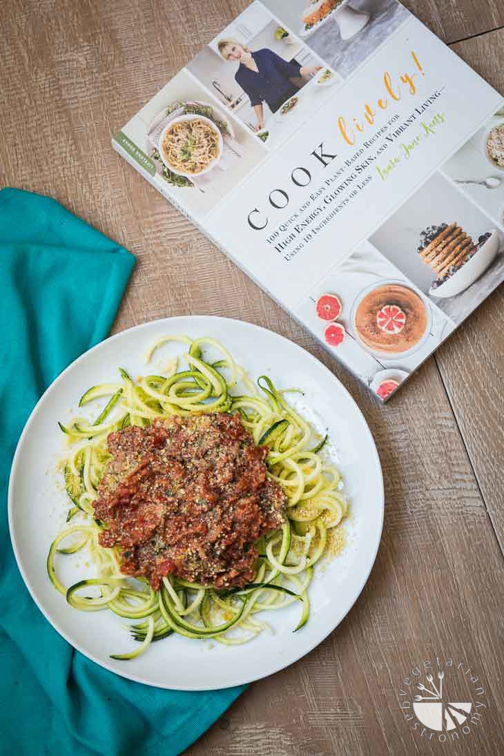 An overhead photograph of a white plate with zoodles and easy spaghetti sauce recipe. There's a cookbook and blue napkin sitting on the side of the plate.