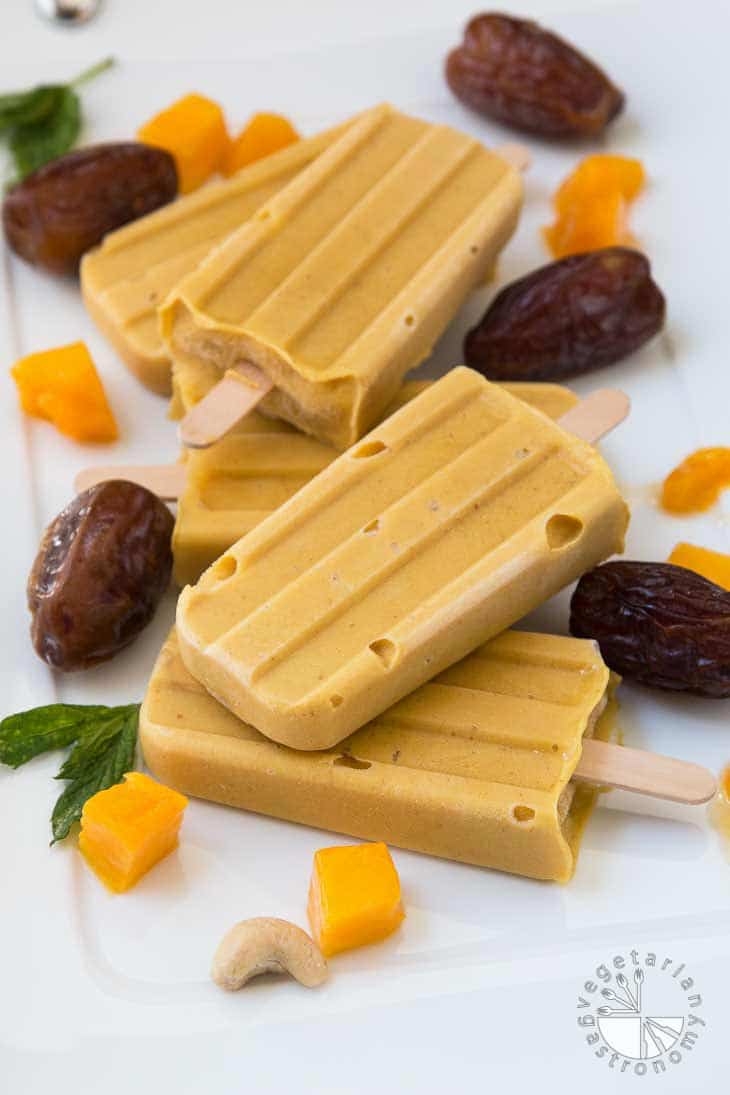 A photography of vegan mango popsicles stacked on top of each other and laying flat on a white tray. 