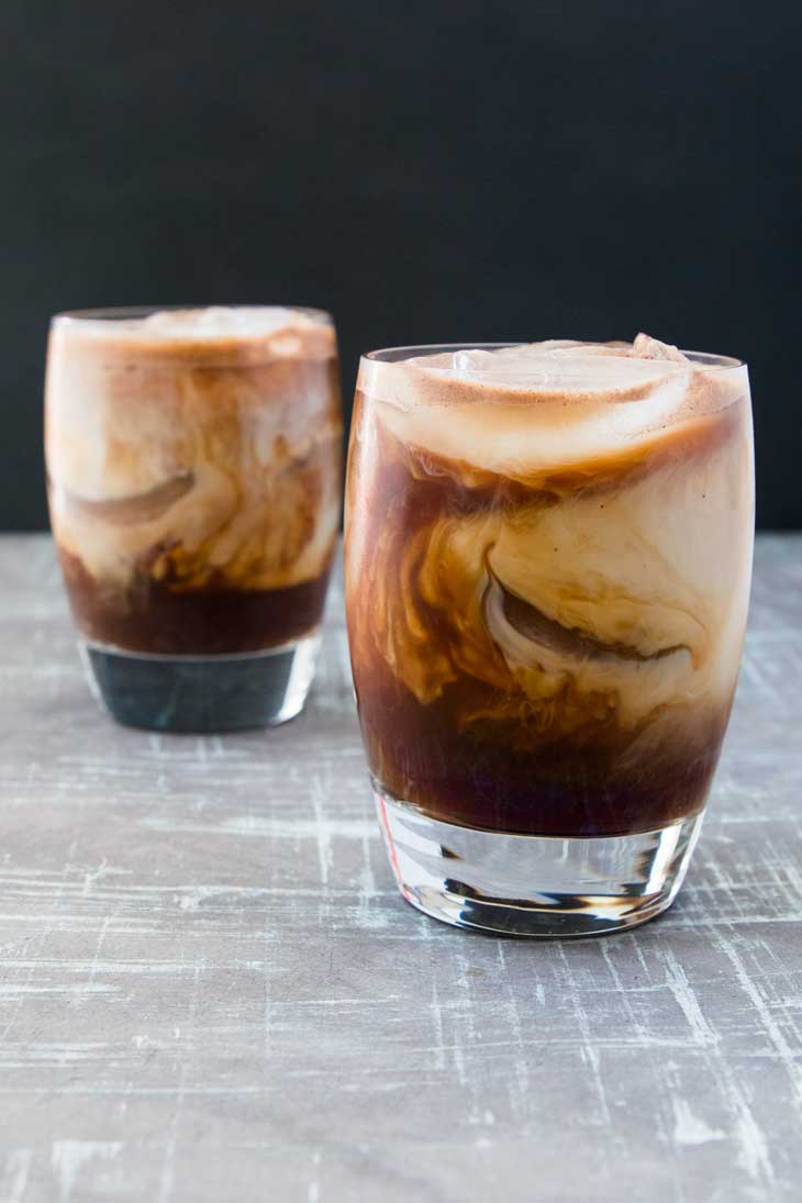 Front photograph of two glass filled with aztec iced mocha recipe. The glasses are sitting on a gray board with black in the background.