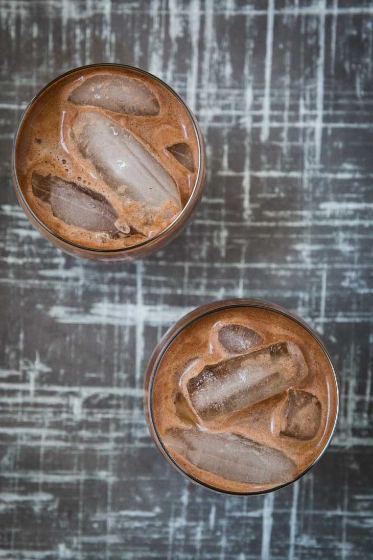 Overhead photograph of two glassed filled with an easy Aztec iced mocha recipe. They are sitting on a gray and white board.