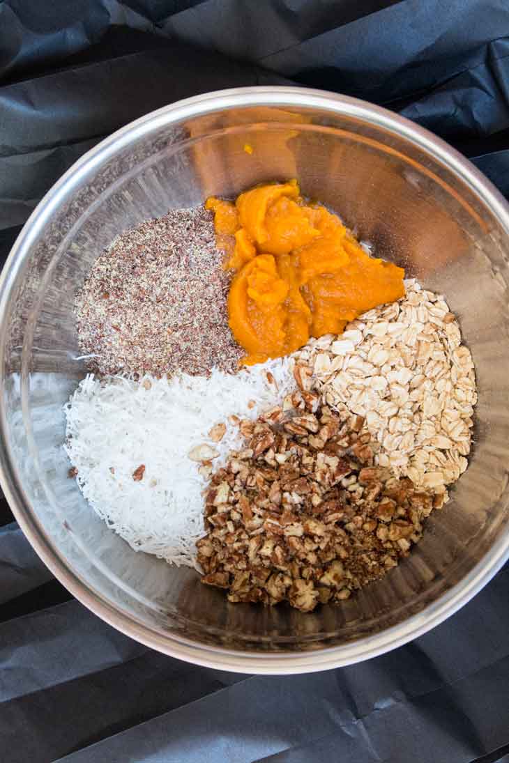 A mixing bowl containing the ingredients to make no-bake vegan pumpkin cookies. There's a steel bowl with flax seeds, coconut, pumpkin puree, pecans, and oats. 