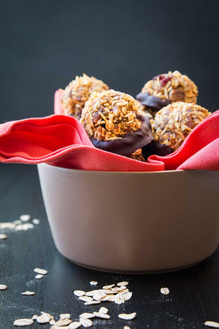 A side view of a tan bowl containing no-bake vegan pumpkin cookies. The bowl is sitting on a black table-top with oats scattered.