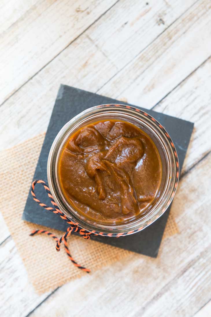 An overhead photograph of vegan 15-minute pumpkin butter recipe sitting in a mason jar on a slate black plate. 