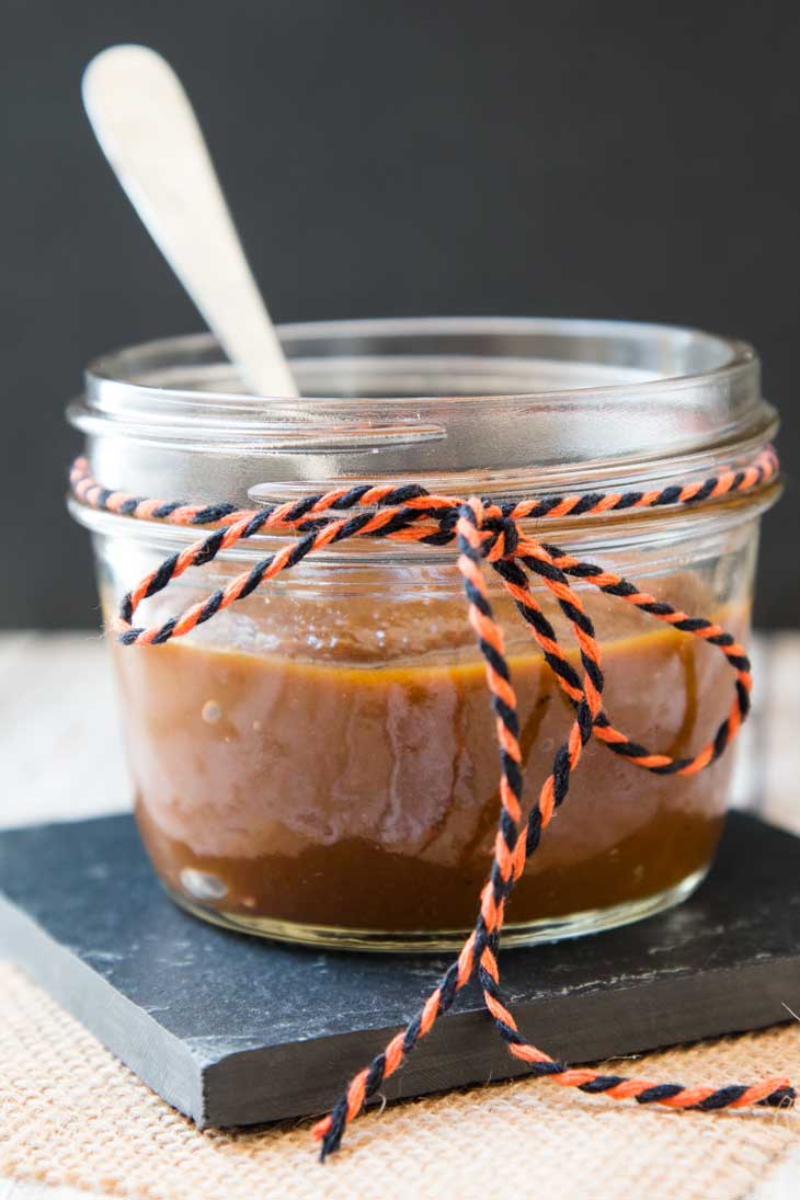 A photograph of vegan pumpkin butter recipe in a small mason jar with an orange and black ribbon tied around it. 